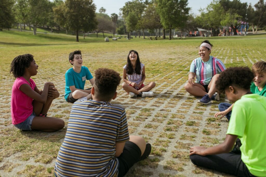 giggling youth sitting outdoors in a circle with an adult leader for group counselling